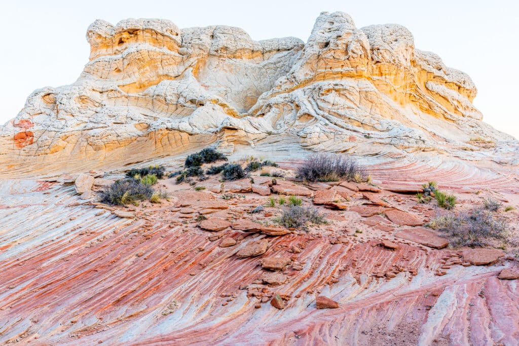Swirling Red and orang rocks make a colorful rock formation with sparse desert bushes growing where they can.