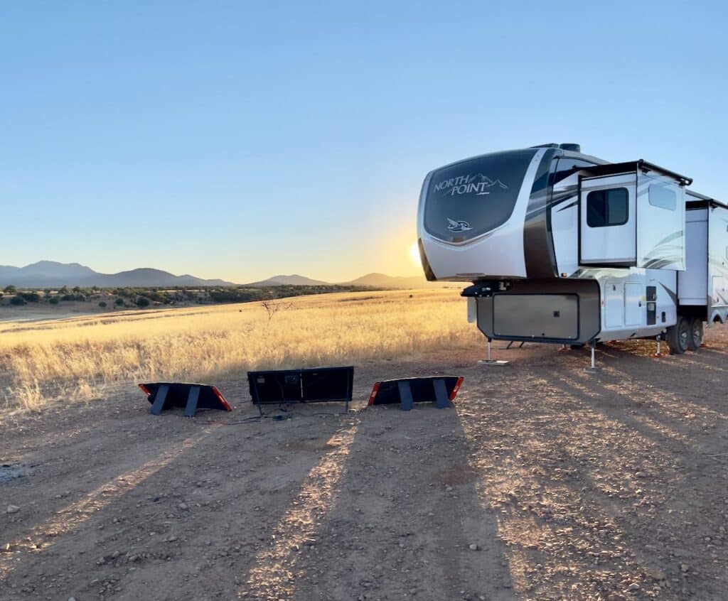 A large camper set up in the sonoran desert with solar panels out facing the setting sun.